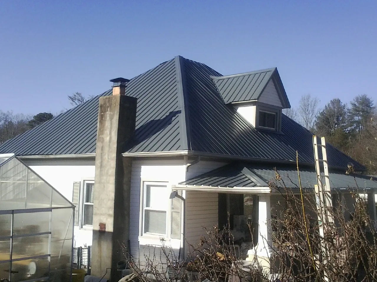 Dark blue standing seam metal roof on a white farmhouse with dormer — Slate & Tile Roof Repair by Roofing Brothers in Bessie