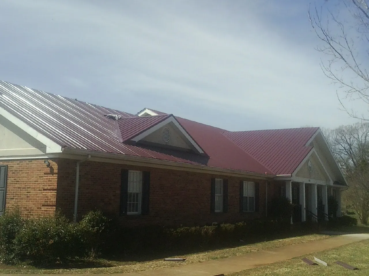 Red metal roof with gabled entries on a long brick building, from a Hail Damage Roof Repair job in Bessie