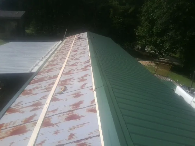 Old rusted panels beside newly installed green metal roofing — Wind Damage Roof Repair by Roofing Brothers in Bessie