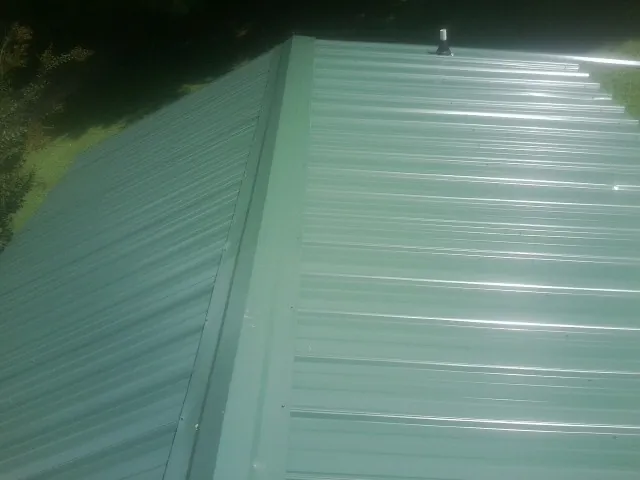 New green metal panels meeting at the ridge of a roof — Flat Roof Repair work by our crew in Bessie