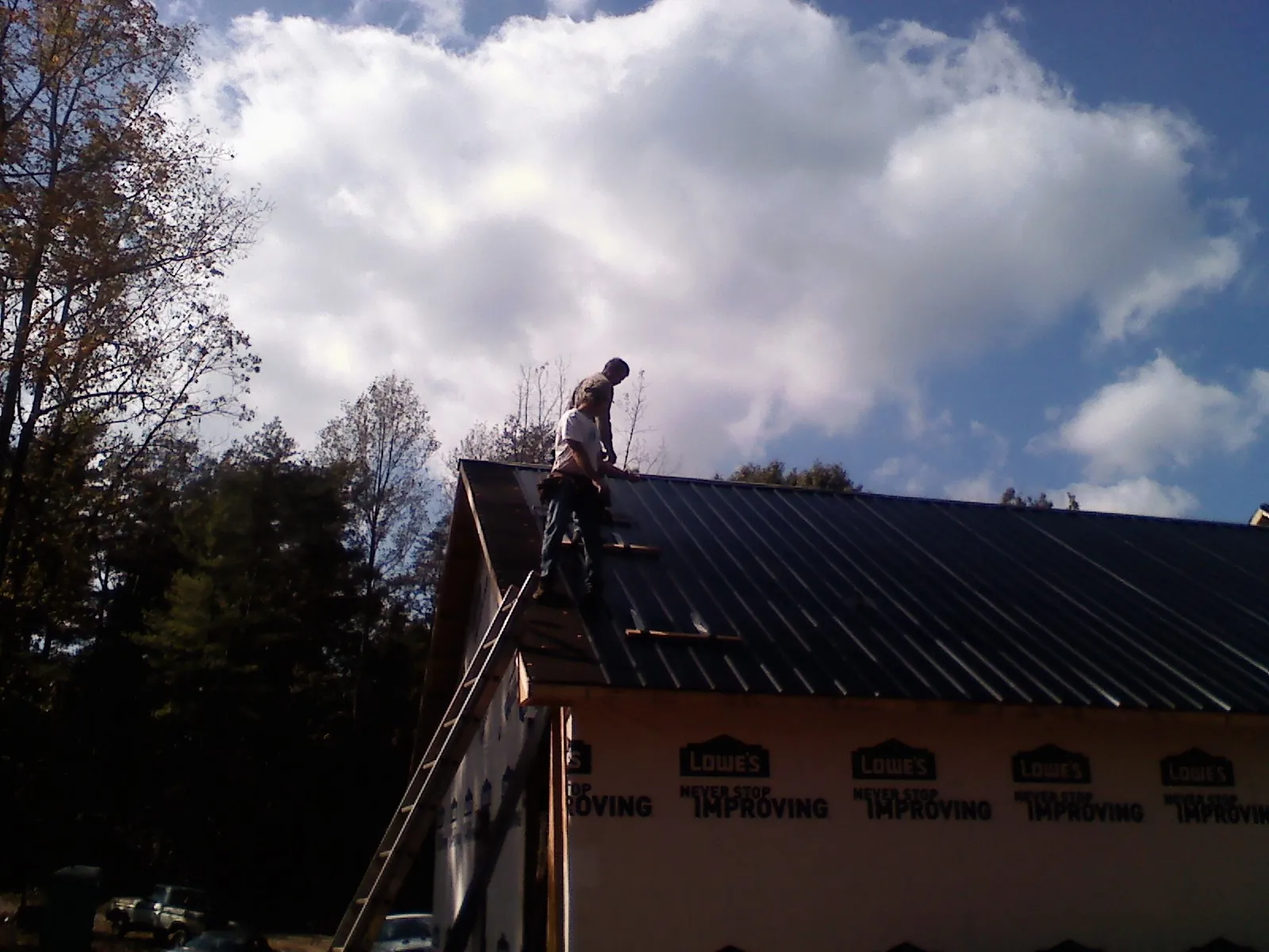 Roofer fastening dark metal panels high against a cloudy sky, from a Roof Inspection job in Bessie