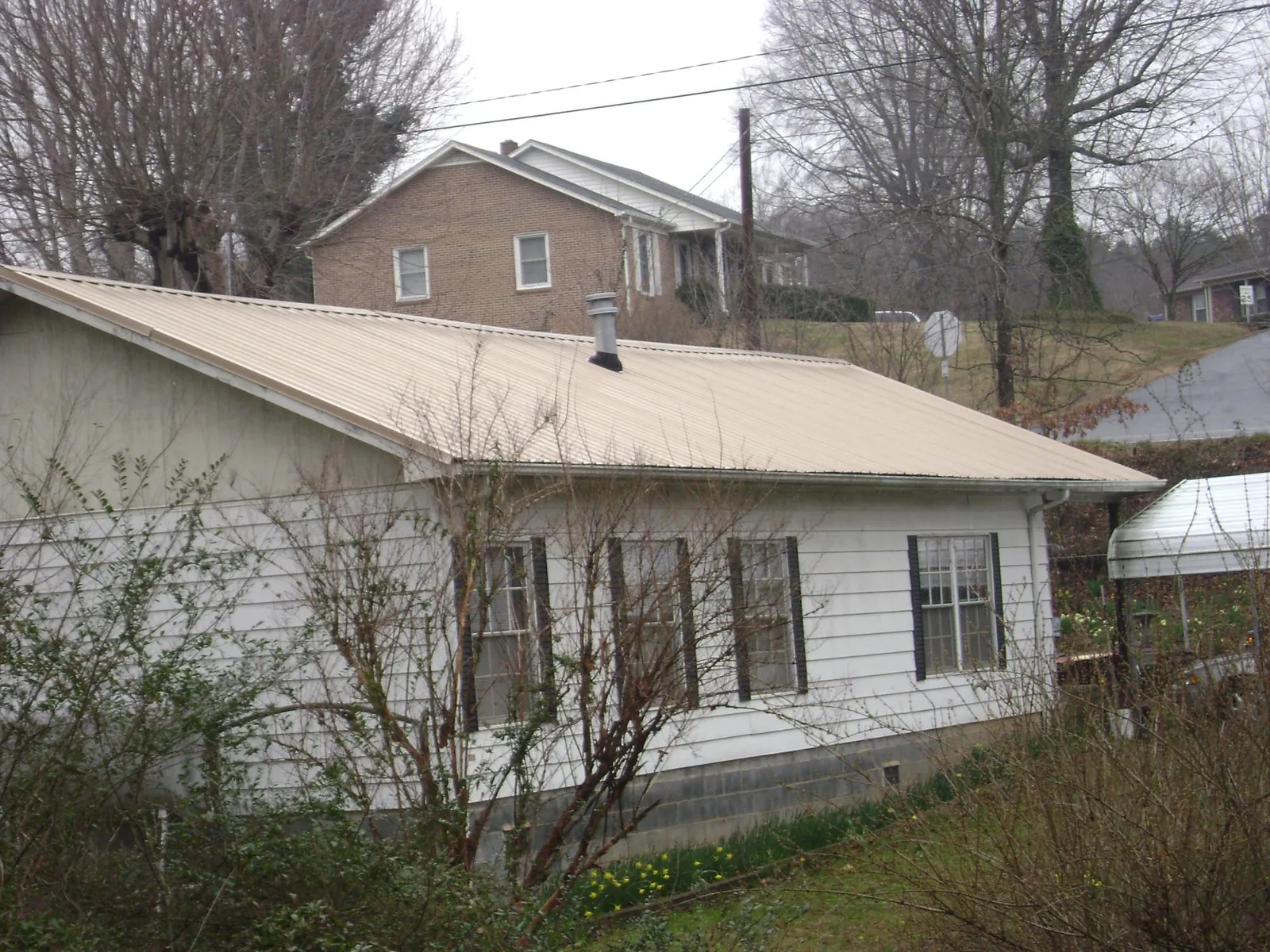Tan metal roof on a white sided house set into a hillside — Commercial Roofing by Roofing Brothers in Bessie