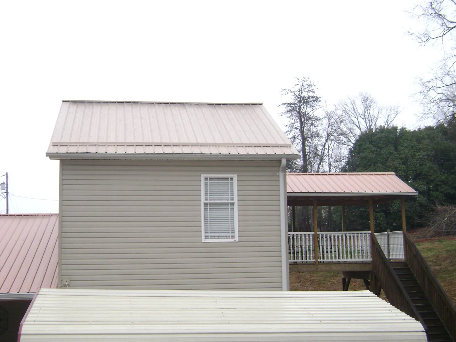 Tan metal roofs on a two story addition and attached porch, from a Roof Replacement job in Bessie