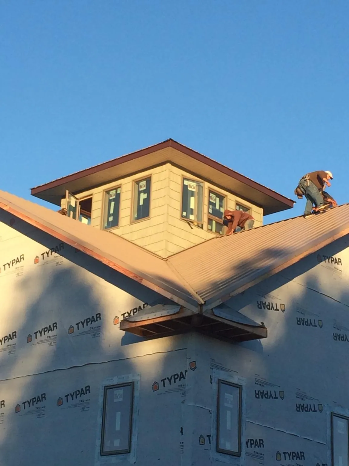 Roofers working around a rooftop cupola on a new metal roof at sunset — Roof Waterproofing in Bessie by Roofing Brothers